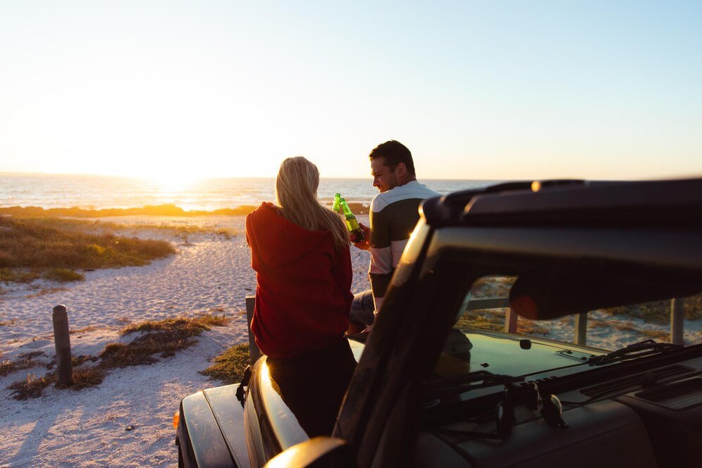 rear-view-caucasian-couple-outside-their-open-top-car-with-sunset-beach-background-making-toast_13339-304203